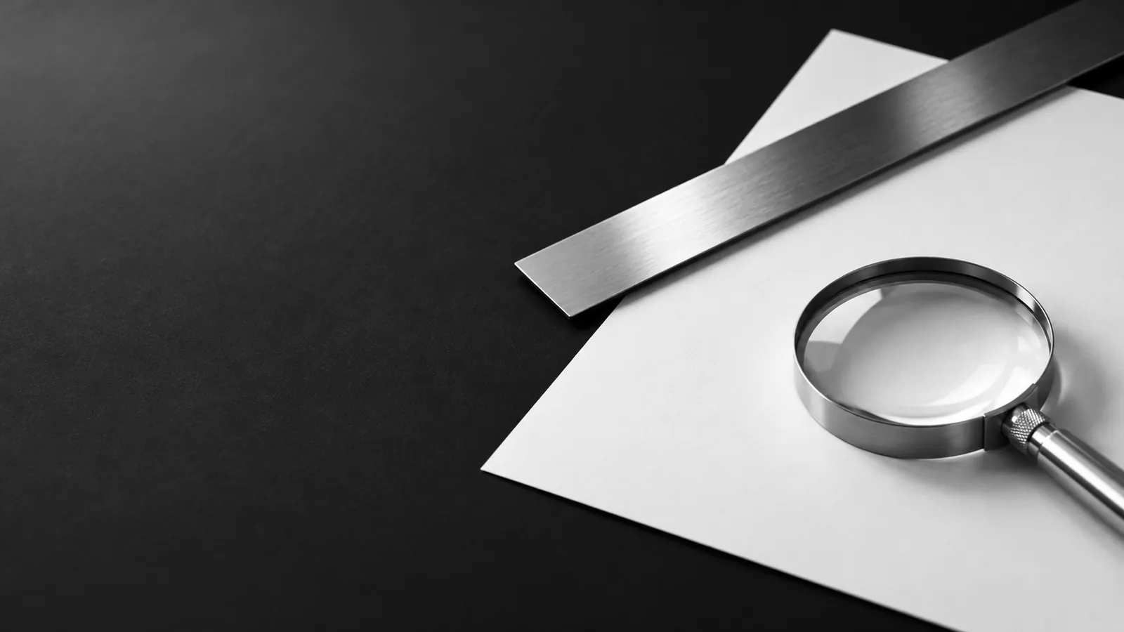 A steel magnifier and cut paper window, inviting a closer look at the evidence.