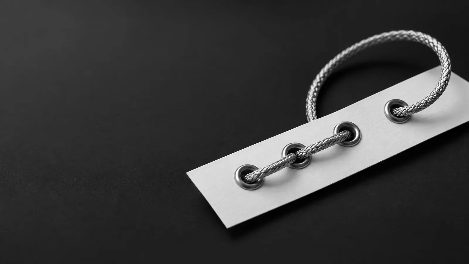 A silver cord threads four steel eyelets on white paper, suggesting a connected workflow.