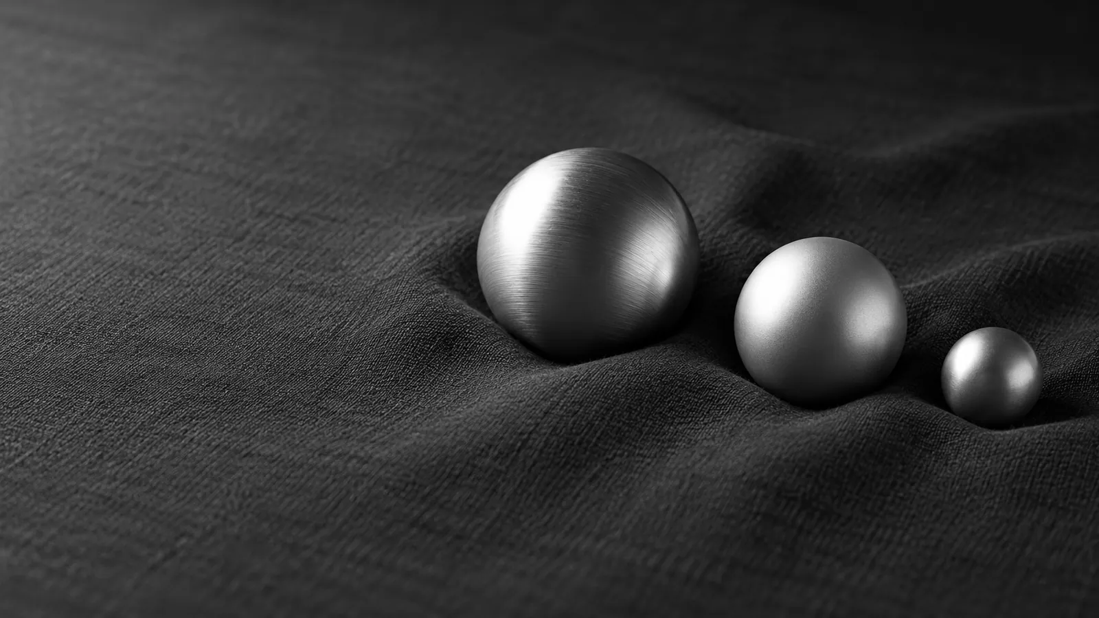Three silver spheres of different sizes rest on charcoal cloth, suggesting measured differences.